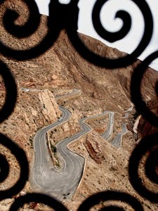 Scenic view of a winding road through the Atlas Mountains framed by ornate ironwork.